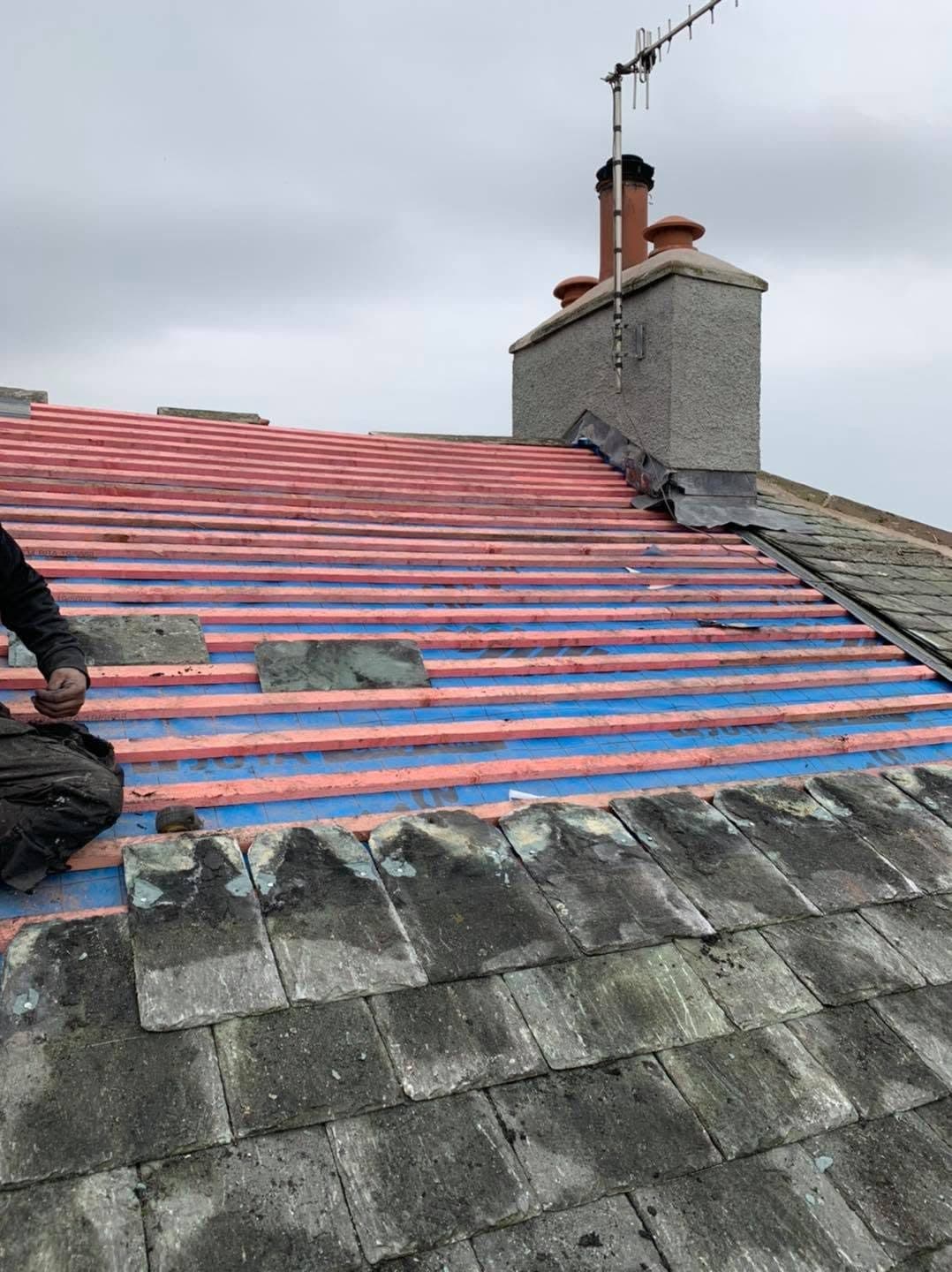 A roof stripped to the rafters and re-covered with blue breather membrane and new treated battens, the old stone slates still in place along the eaves and fresh lead dressed into the chimney.