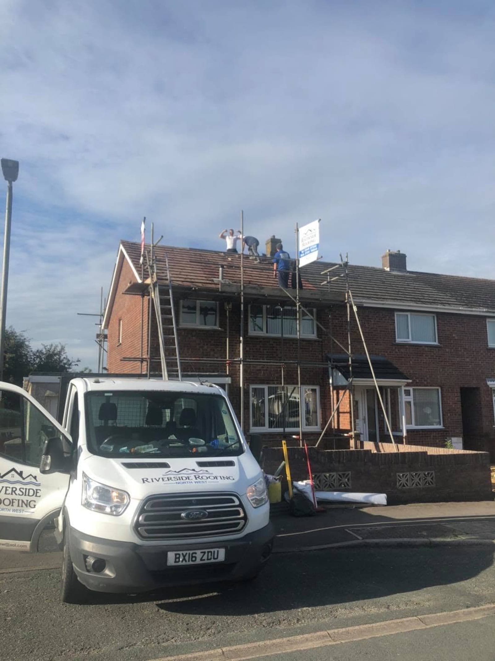Three roofers stripping a semi-detached roof on a clear day, with scaffolding up and the company van parked at the kerb.