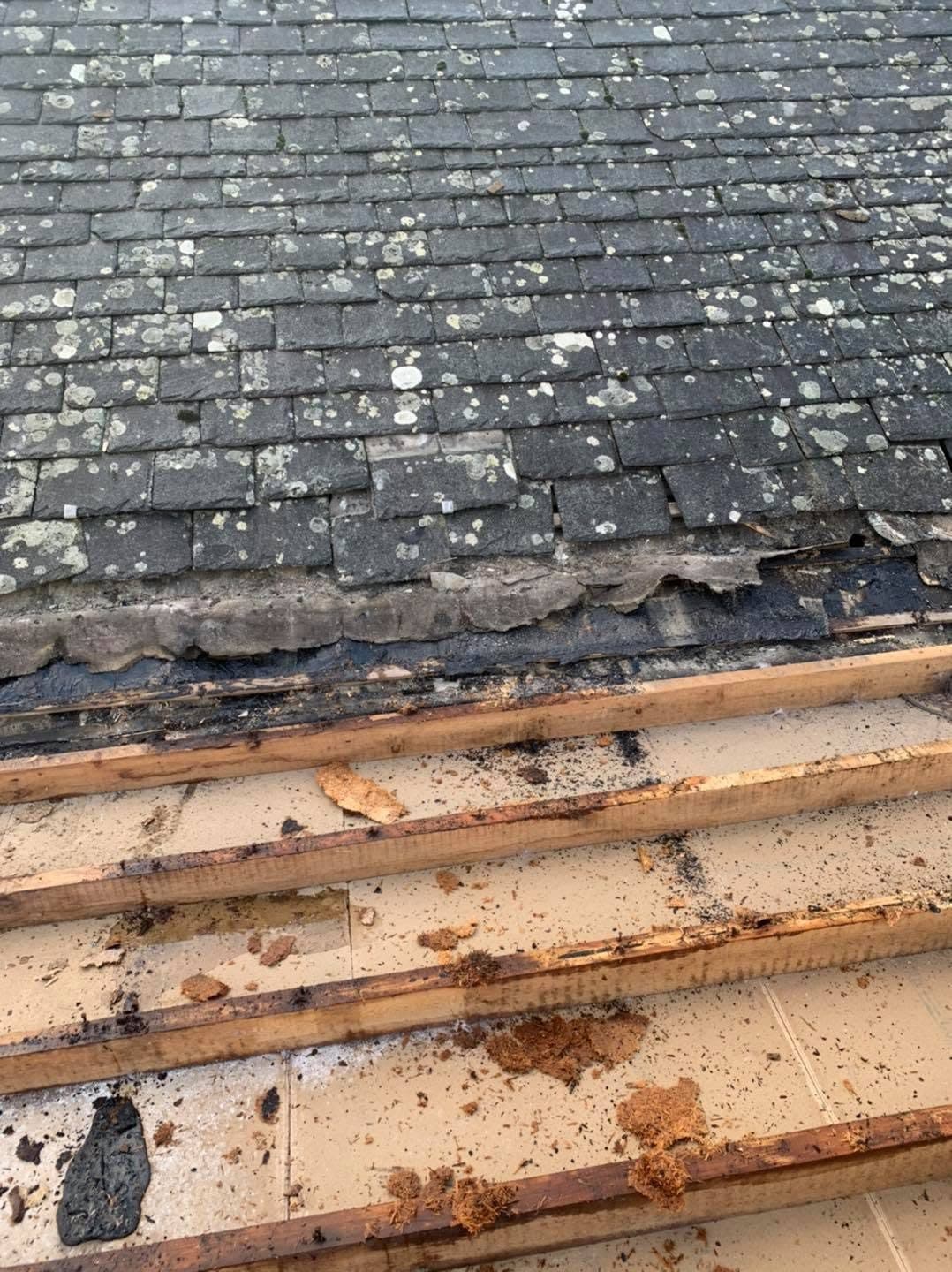 A slate roof stripped back at the eaves, showing perished felt and rotten, crumbling timbers underneath the bottom courses.