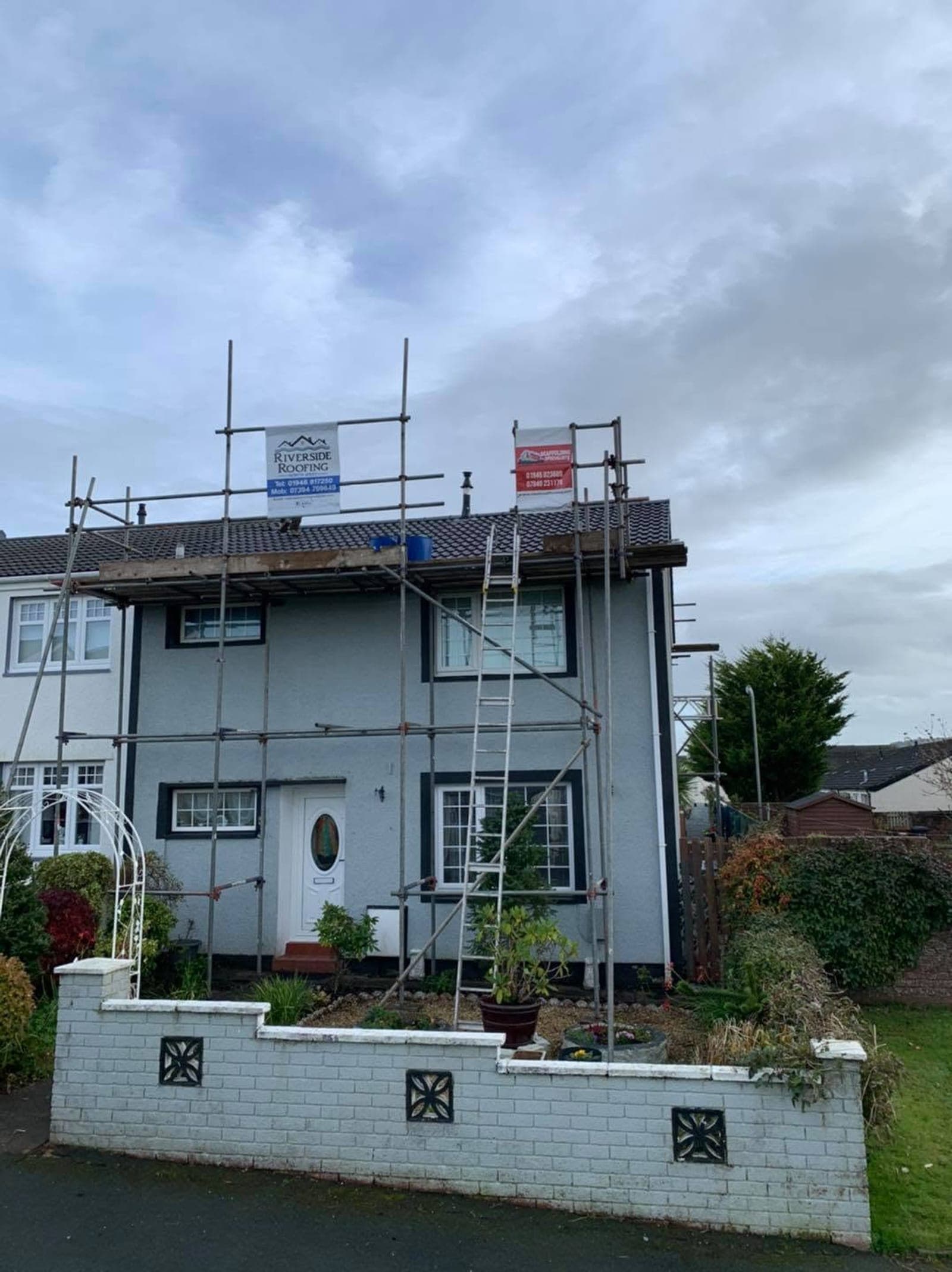 Scaffolding around a pale blue rendered house with a newly finished tiled roof.