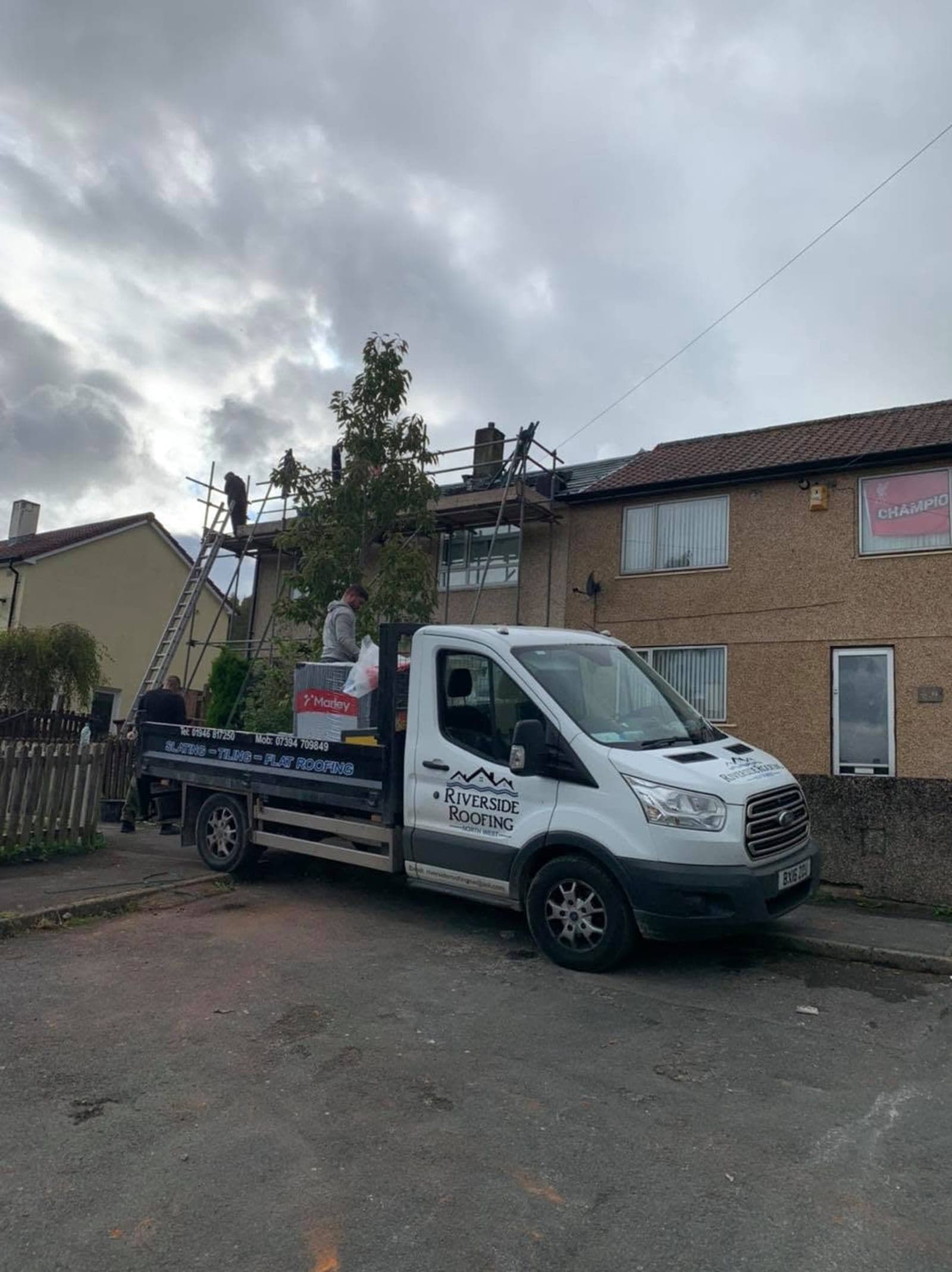 The company van loaded with pallets of new tiles outside a house with the roof stripped back.