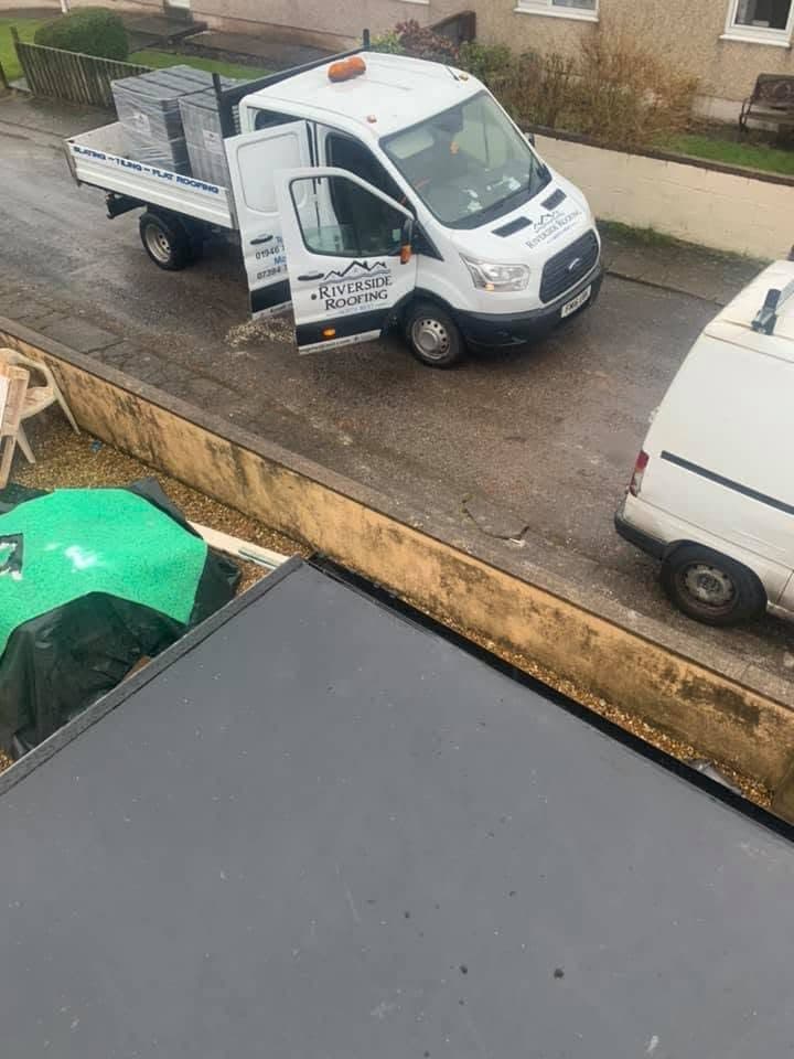 The Riverside Roofing tipper on a driveway loaded with banded pallets of slate, seen from the flat roof being worked on.